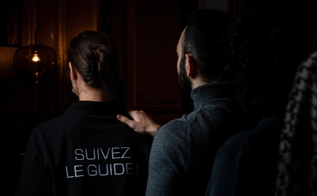 Un homme suit une guide dans un espace sombre, la main posée sur son épaule, lors d’une expérience immersive Dans le Noir ?